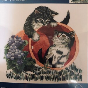Puede incluir: Patrón de bordado con dos gatitos juguetones asomándose desde una maceta roja con un racimo de uvas moradas. El patrón se llama "Playful Kittens" y es de Janlynn.com.