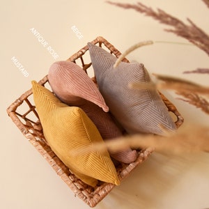 View from above: set of three pillows rest in wicker basket. They all make a bohemian set made of corduroy fabrics in beige, pink and mustard color.
