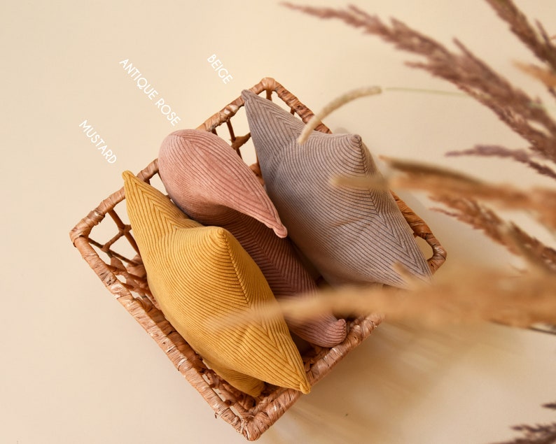 View from above: set of three pillows rest in wicker basket. They all make a bohemian set made of corduroy fabrics in beige, pink and mustard color.