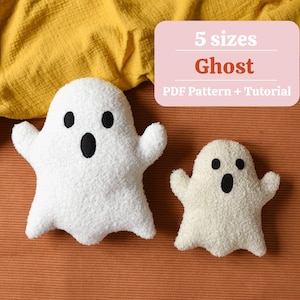 Könnte beinhalten: Zwei weiße, plüschige Geisterkissen mit schwarzen Augen und Mündern. Der größere Geist befindet sich links und der kleinere rechts. Ein rosa Rechteck im Hintergrund zeigt "5 Größen Ghost PDF Pattern + Tutorial."