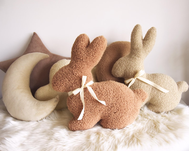 May include: Two plush brown bunny rabbit toys with cream colored ribbon bows, and a cream colored crescent moon shaped pillow with brown corduroy trim.