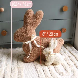 May include: Two plush bunny rabbit toys on a white rug. The larger bunny is brown and measures 16.5 inches tall. The smaller bunny is white with black polka dots and measures 8 inches tall.