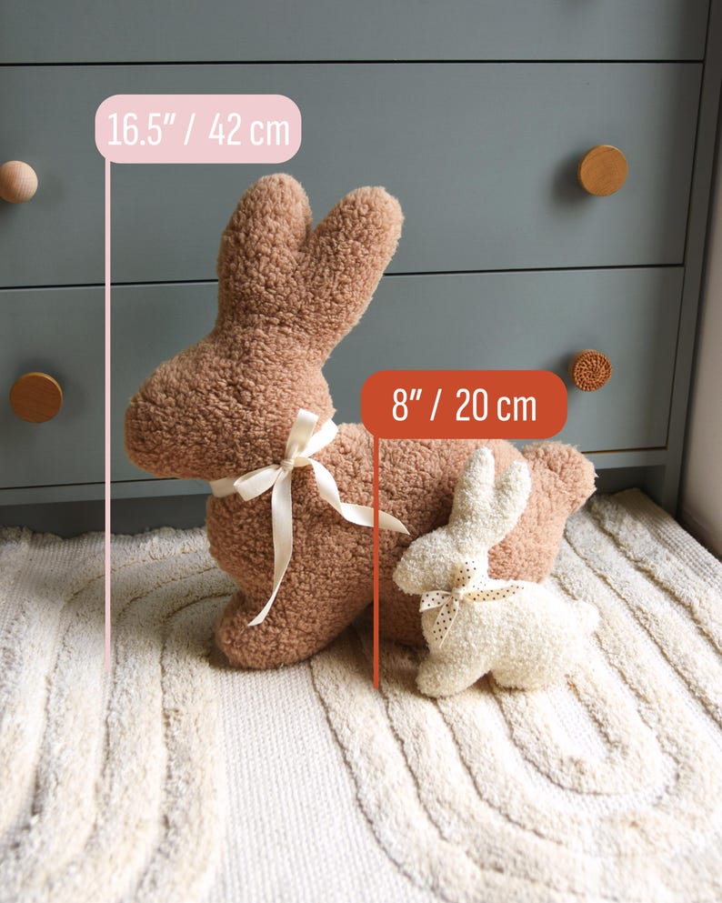 May include: Two plush bunny rabbit toys on a white rug. The larger bunny is brown and measures 16.5 inches tall. The smaller bunny is white with black polka dots and measures 8 inches tall.