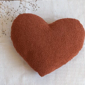 May include: A heart-shaped pillow made of a soft, fuzzy, rust-colored fabric.