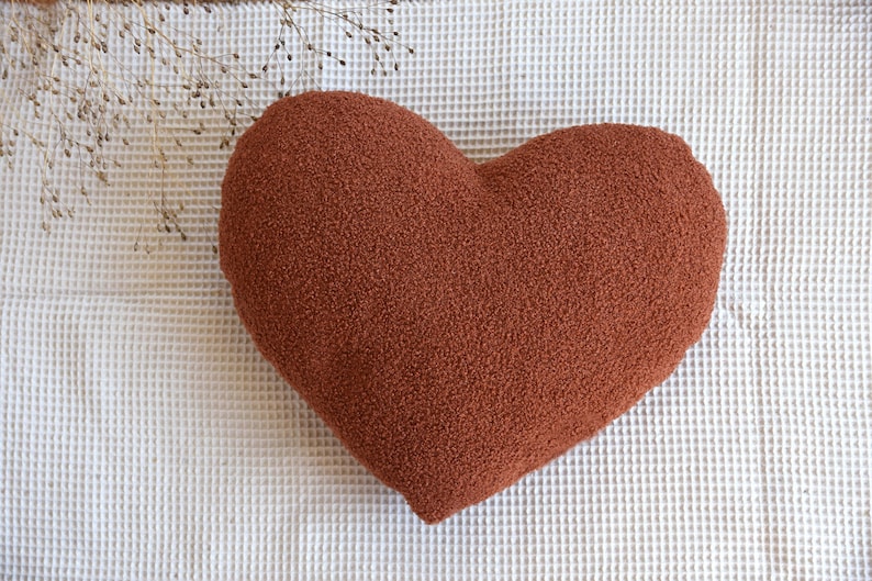 May include: A heart-shaped pillow made of a soft, fuzzy, rust-colored fabric.
