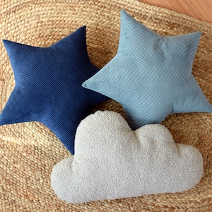 May include: Three decorative pillows in the shape of a star and a cloud. The star pillows are made of a blue corduroy fabric. The cloud pillow is made of a fluffy, white fabric.