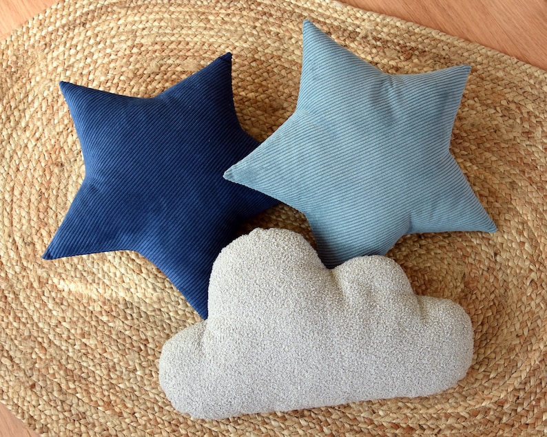 May include: Three decorative pillows in the shape of a star and a cloud. The star pillows are made of a blue corduroy fabric. The cloud pillow is made of a fluffy, white fabric.