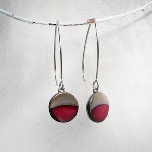 May include: A pair of silver dangle earrings with round, red and gray ceramic pendants.