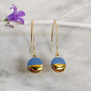 Può includere: Un paio di orecchini pendenti dorati con ciondoli rotondi in ceramica blu e oro. I ciondoli sono metà blu e metà oro.