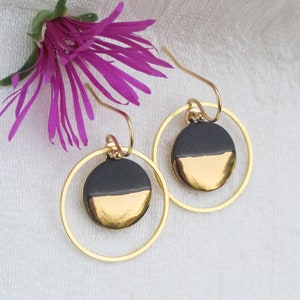 May include: A pair of gold hoop earrings with black and gold ceramic discs. The discs are half black and half gold.