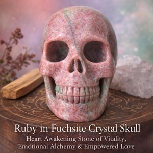 May include: A carved ruby in fuchsite crystal skull. The skull is pink with green veining and detailed teeth. The text at the bottom reads "Ruby in Fuchsite Crystal Skull" and "Heart Awakening Stone of Vitality, Emotional Alchemy & Empowered Love."
