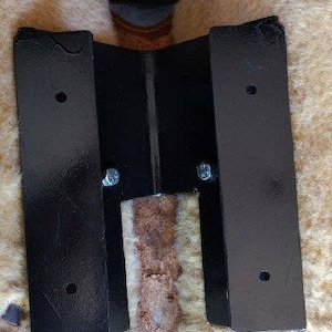 May include: Two black metal brackets with screw holes and a center support bar. The brackets are attached to a beige fabric surface.