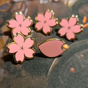 Peut inclure: Cinq épingles de couleur or avec émail rose. Quatre épingles sont en forme de fleurs de cerisier et une est un seul pétale de fleur de cerisier.