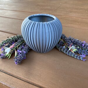 May include: A gray ceramic planter with a ribbed design, sitting on a wooden surface with lavender flowers.