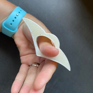 May include: White plastic finger splint with a textured surface. The splint is designed to support the thumb.