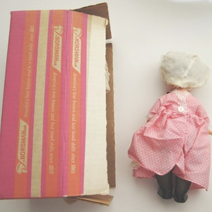 May include: A pink and white polka dot dress with a white lace trim and a white bonnet. The dress is on a box with the text "HORSMAN America's best known and best loved dolls since 1865" printed on it.