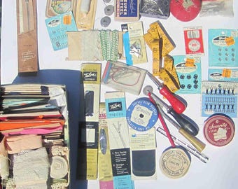 May include: A collection of vintage sewing supplies including Talon zippers, Braid-Aid folders, spools of thread, a red tomato pincushion, a yellow measuring tape, various metal fasteners, needles, seam rippers, and a box filled with assorted ribbons and lace.