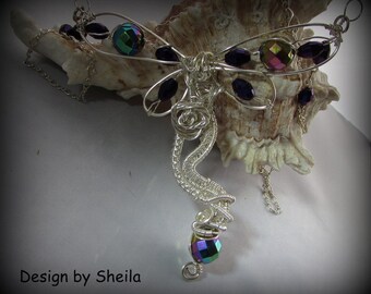 May include: A silver wire wrapped dragonfly pendant necklace with iridescent purple and green glass beads. The necklace is displayed on a seashell.