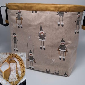 Puede incluir: Una bolsa de cordón beige con una parte superior marrón y un patrón de niñas pequeñas con ropa de invierno. La bolsa tiene una correa negra.