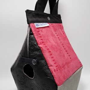 Op de afbeelding: Een unieke draagtas met een geometrisch ontwerp. De tas heeft zwart leer met reliëfskulls, een roze suède paneel en een grijs paneel met skull-afdrukken. Het heeft een zwart handvat en een label met "FiberRocker".