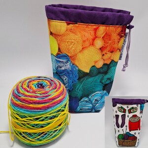 May include: A colorful yarn ball next to a drawstring project bag. The bag features a vibrant print of yarn balls in shades of orange, yellow, and teal, with a purple rim. A smaller bag with knitting-themed illustrations is also visible.