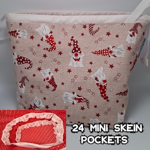 Puede incluir: Una bolsa de almacenamiento de tela beige con forro blanco y un patrón de gnomo rojo y blanco. La bolsa tiene 24 bolsillos para mini ovillos y el texto "24 MINI SKEIN POCKETS" está impreso en la parte delantera.