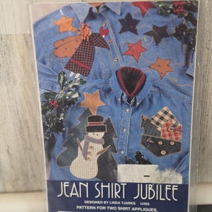 May include: A craft pattern packet titled Jean Shirt Jubilee featuring two blue denim shirts decorated with fabric appliques. One shirt displays a snowman and stars, while the other features a winged figure and stars. The cover includes text and images.