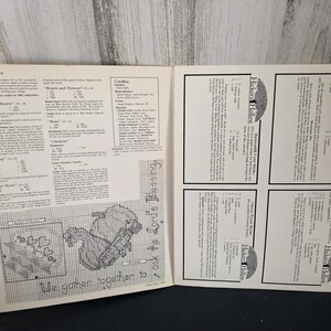May include: Open book with pages featuring cross-stitch patterns and project notes. The text "We gather together to ask the Lord's Blessing" is visible. The book also includes the text "Hickory Hollow".
