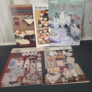 May include: A collection of vintage craft pattern books. Titles include "Bread Covers," "Bordering," "Soft & Sweet Basket Cloths," "Christmas Best Breadcovers and Recipes," and "Sunday Best Breadcovers and Recipes." The covers feature images of embroidered and crocheted items.