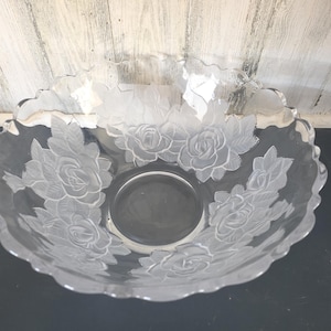 May include: A clear glass bowl with a scalloped edge and etched rose design. The bowl has a circular base and is decorated with detailed floral patterns. The bowl is suitable for serving or display.