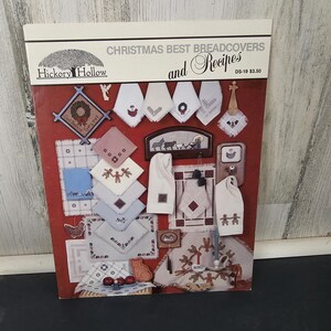 May include: A book cover titled "Christmas Best Breadcovers and Recipes" by Hickory Hollow. The cover is red with various embroidered Christmas-themed designs, including wreaths, snowflakes, and gingerbread people. The book is a collection of bread cover patterns and recipes.