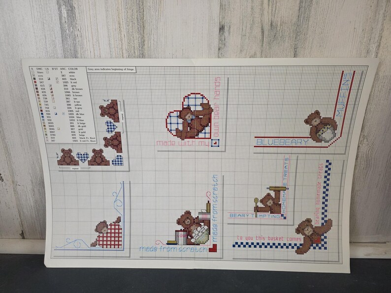 Op de afbeelding: Een kruissteekpatroonvel met teddybeerontwerpen. De vel bevat verschillende teddybeermotieven, harten en tekstelementen zoals "made with my own bear hands" en "blueberry treats". Het kleurenpalet omvat bruin, rood en blauw.