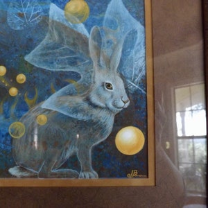 May include: A painting of a white rabbit with a blue and white patterned wing, surrounded by yellow and white orbs on a blue background.