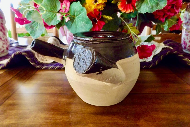 May include: A brown and beige ceramic teapot with a unique spout and a decorative design. The teapot is sitting on a wooden table.