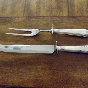 May include: A silver carving set with a knife and fork. The handles are decorated with an ornate pattern.