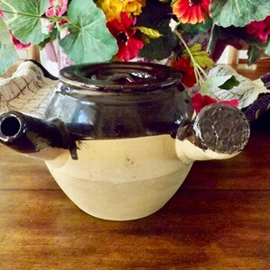 May include: A brown and beige ceramic teapot with a dark brown lid and a spout on the side. The teapot has a handle on the side and a smaller handle on the opposite side.