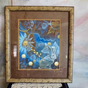 May include: A framed art print featuring a white rabbit with large ears and a crown, surrounded by blue and gold abstract shapes and leaves.