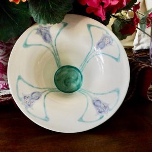 May include: White ceramic bowl with a central green glass knob. The bowl is decorated with blue floral designs and teal accents. The bowl is likely used for decorative purposes.