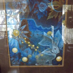 May include: A framed painting of a blue rabbit with large ears in a forest setting. The rabbit is surrounded by blue and yellow leaves and glowing orbs.