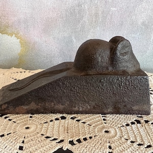 May include: A dark brown, cast iron doorstop with a textured surface. The doorstop features a rounded top and a sloped base with a curved design. The doorstop is designed to prevent doors from closing.