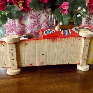 Puede incluir: Un cami&oacute;n de juguete de madera rojo, amarillo y azul con detalles pintados. El cami&oacute;n tiene cuatro ruedas y est&aacute; hecho de madera. El cami&oacute;n est&aacute; sobre una superficie de madera.