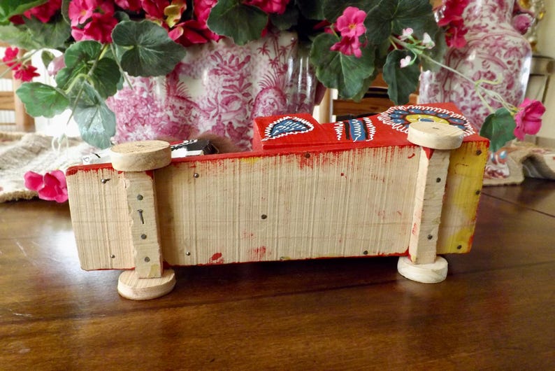 Puede incluir: Un cami&oacute;n de juguete de madera rojo, amarillo y azul con detalles pintados. El cami&oacute;n tiene cuatro ruedas y est&aacute; hecho de madera. El cami&oacute;n est&aacute; sobre una superficie de madera.