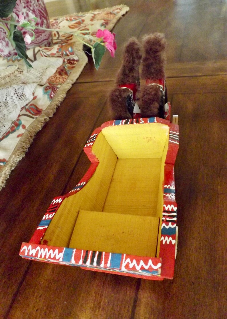 Puede incluir: Un carro de juguete de madera con dos caballos de peluche marrones tirando de &eacute;l. El carro est&aacute; pintado de rojo con rayas amarillas, azules y blancas.