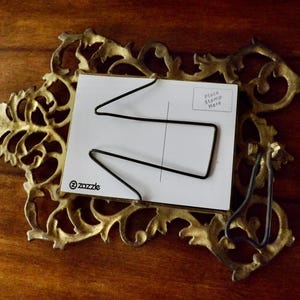 May include: Ornate gold-colored metal postcard holder with a white postcard. The postcard has a black wire design and the text "Place Stamp Here". The Zazzle logo is visible on the postcard.