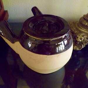 May include: A brown and white ceramic teapot with a unique spout and lid. The teapot has a glossy brown glaze on the top half and a matte white glaze on the bottom half.