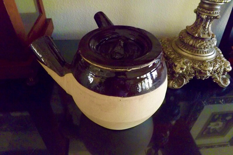 May include: A brown and white ceramic teapot with a unique spout and lid. The teapot has a glossy brown glaze on the top half and a matte white glaze on the bottom half.