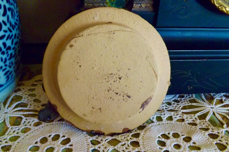 May include: A round, cream-colored ceramic plate with a raised rim and a slightly textured surface. The plate has a worn, vintage look.