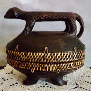 May include: A dark brown wooden box with a carved animal handle and a woven rattan lid. The box is sitting on a white crocheted doily.