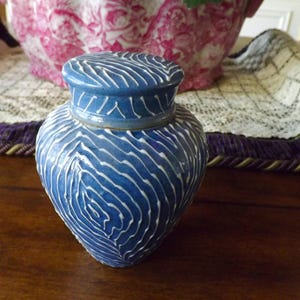 May include: A blue ceramic jar with a white swirl pattern. The jar has a lid and is sitting on a wooden surface.