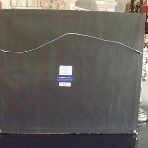 May include: The back of a framed picture with a black mat and a gold frame. A small blue label with white text is attached to the back of the frame. The label reads "Sterling Classics".